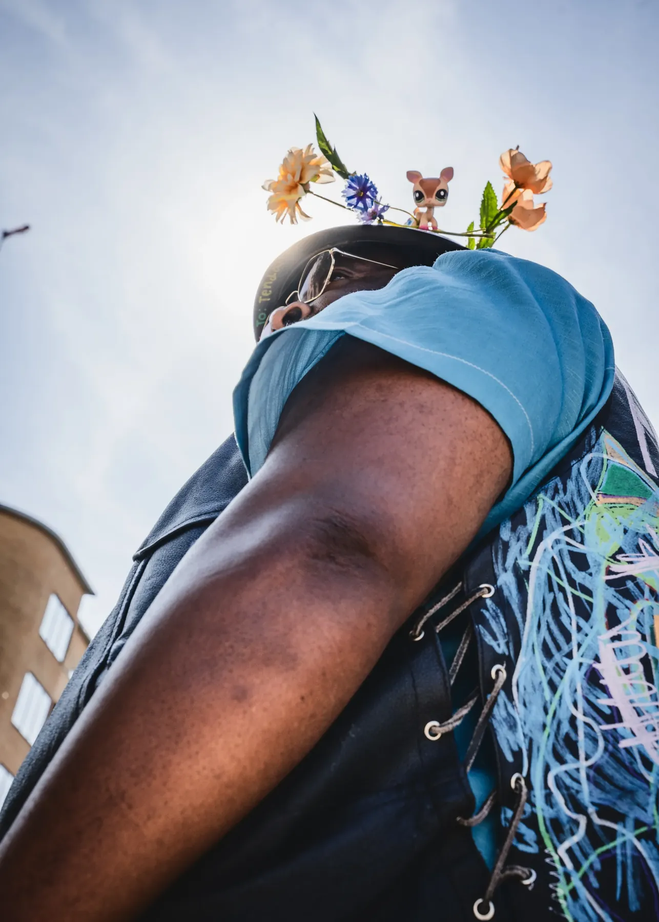 Set nedefra mod himlen: den blomsterdækkede hjelm med et lille plastikdyr øverst og et blåt tørklæde for ansigtet.