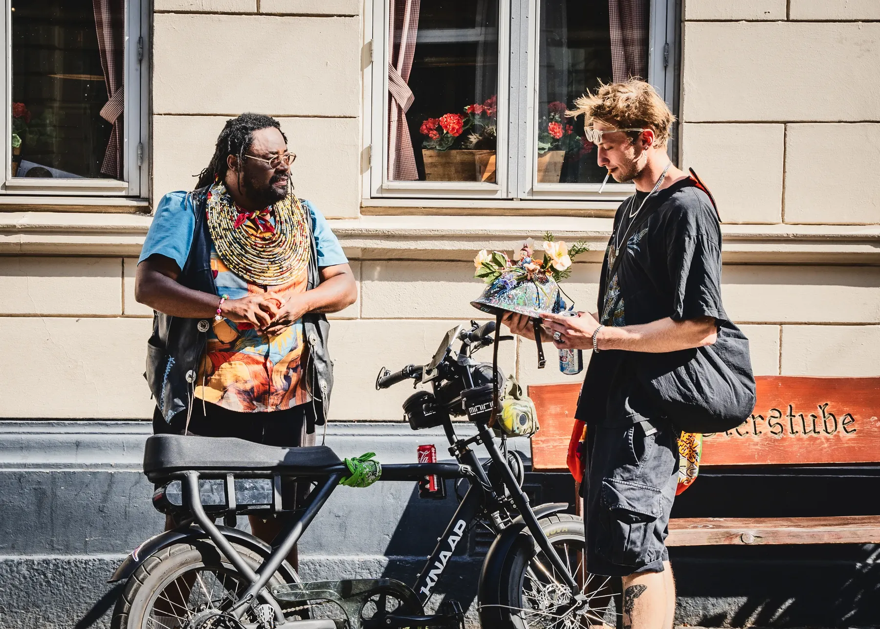 En ung mand på gaden holder den blomsterdækkede hjelm med begge hænder og studerer den, mens FatbikeHero står og ser til.